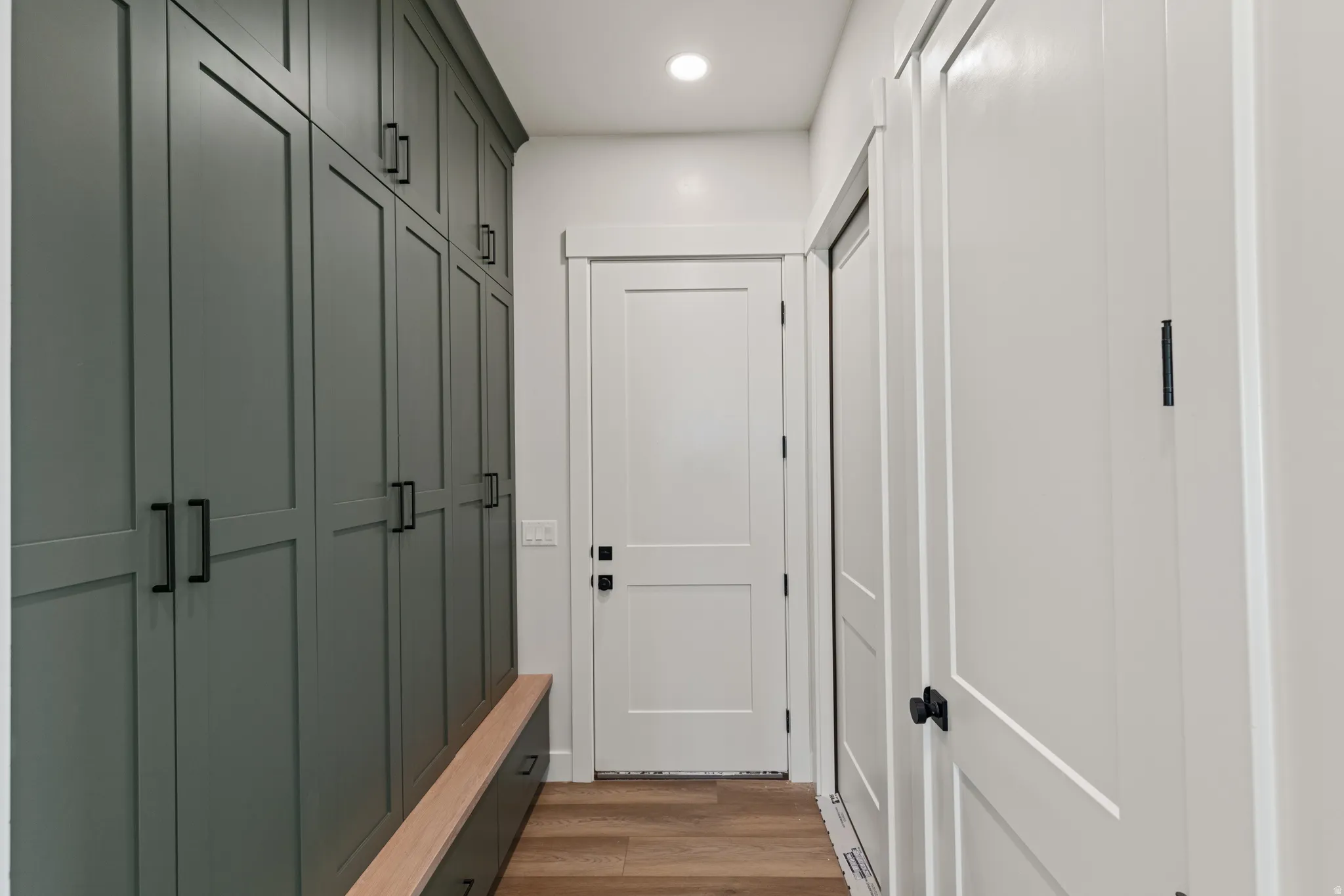 Floor-to-ceiling built-in cabinetry with matte black hardware, integrated wooden bench, light wood-finish flooring, and recessed ceiling lighting