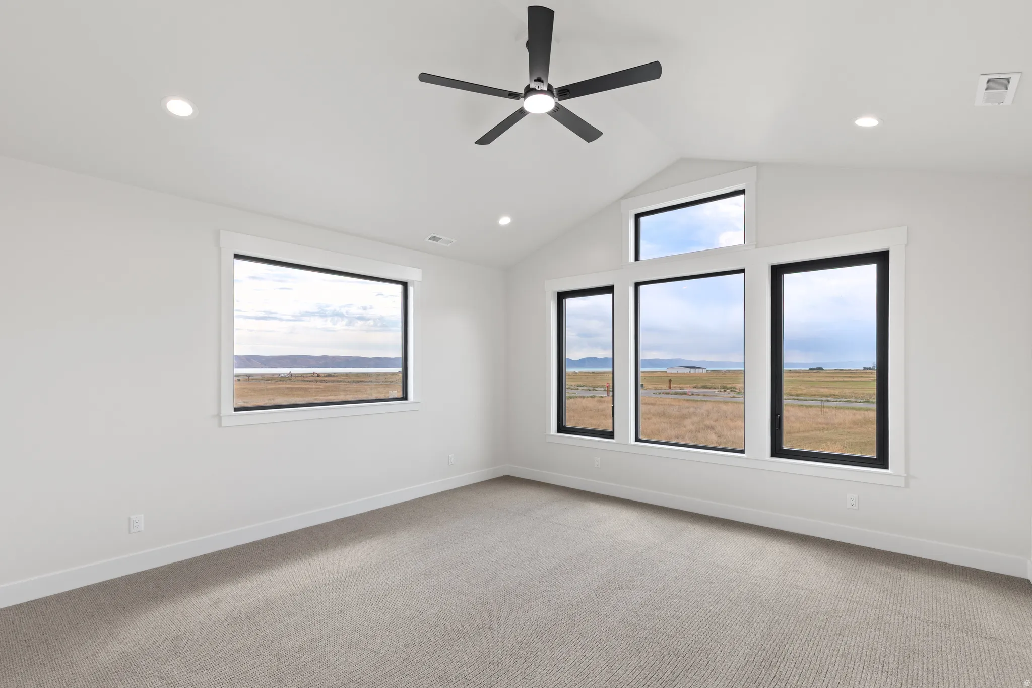Angled vaulted ceiling with recessed lighting, modern ceiling fan, multiple large windows, and carpeted flooring