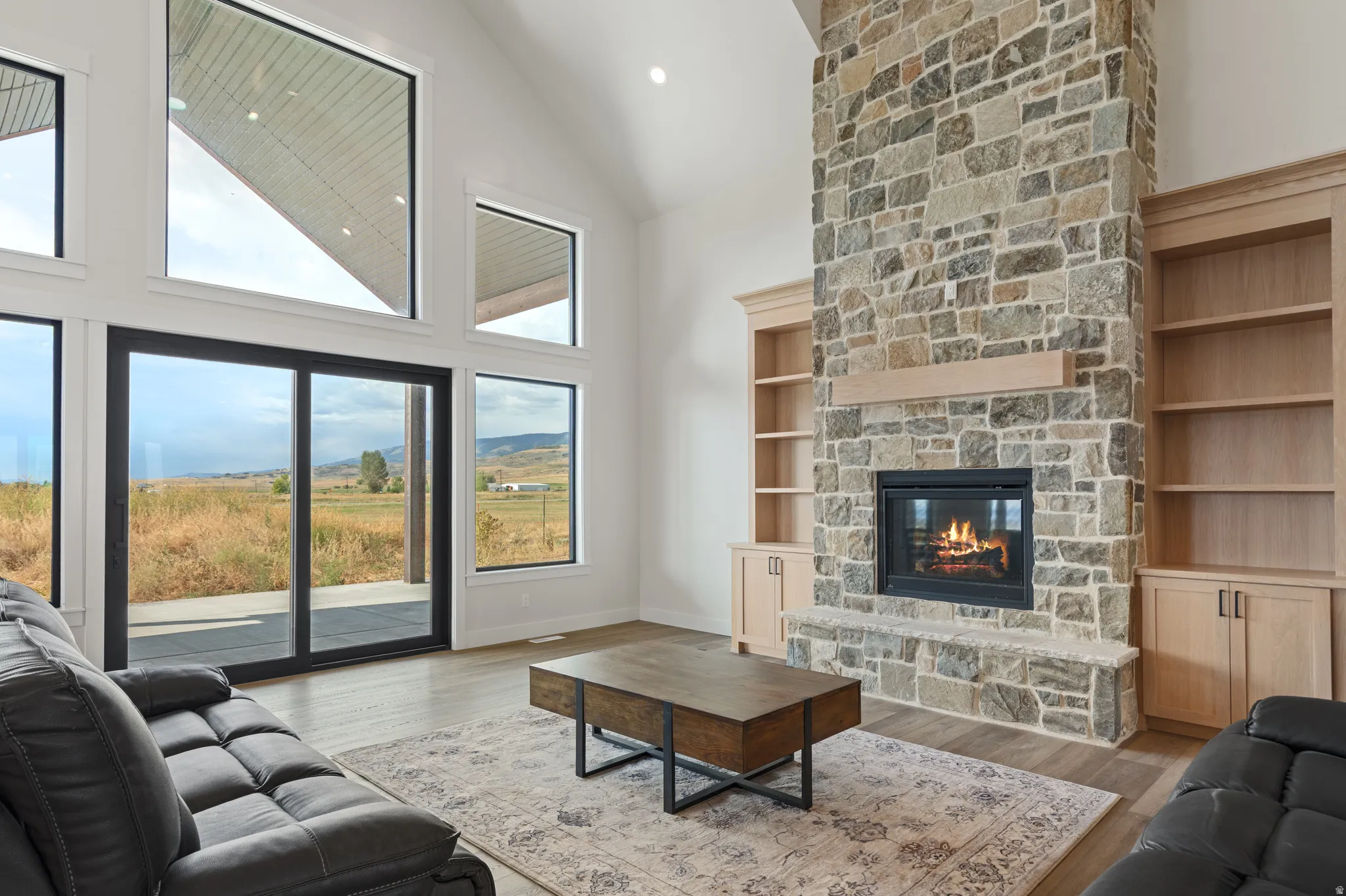 Soaring vaulted ceiling, floor-to-ceiling stone fireplace, built-in shelving, expansive windows, and wood-finish flooring