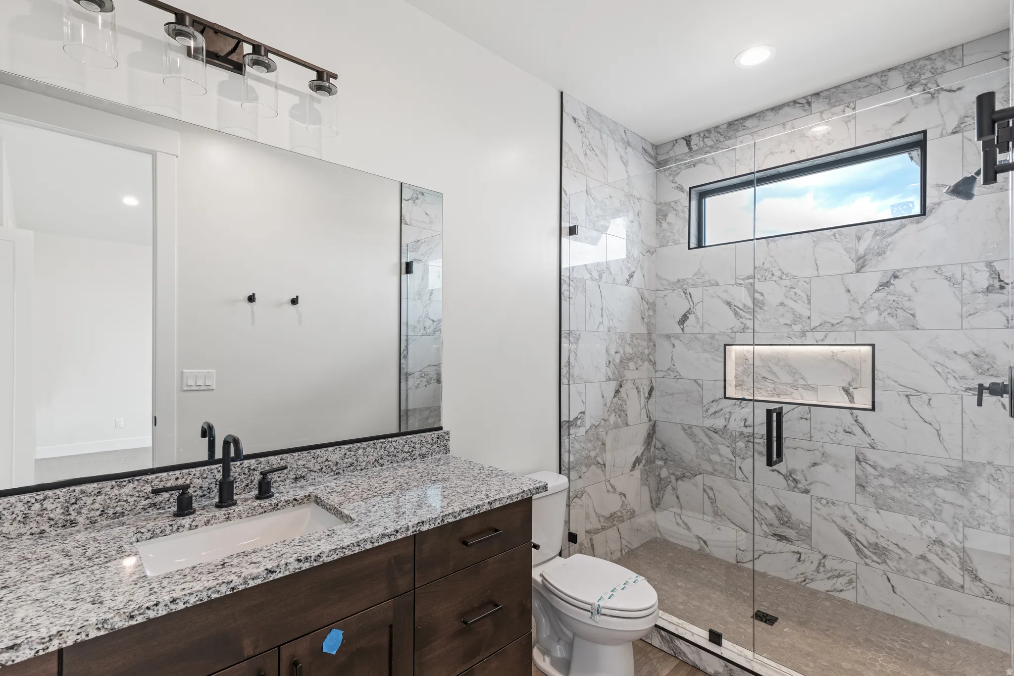 Spacious bathroom featuring a dark wood-finish vanity with a stone countertop, an undermount sink with matte black fixtures, and a large mirror