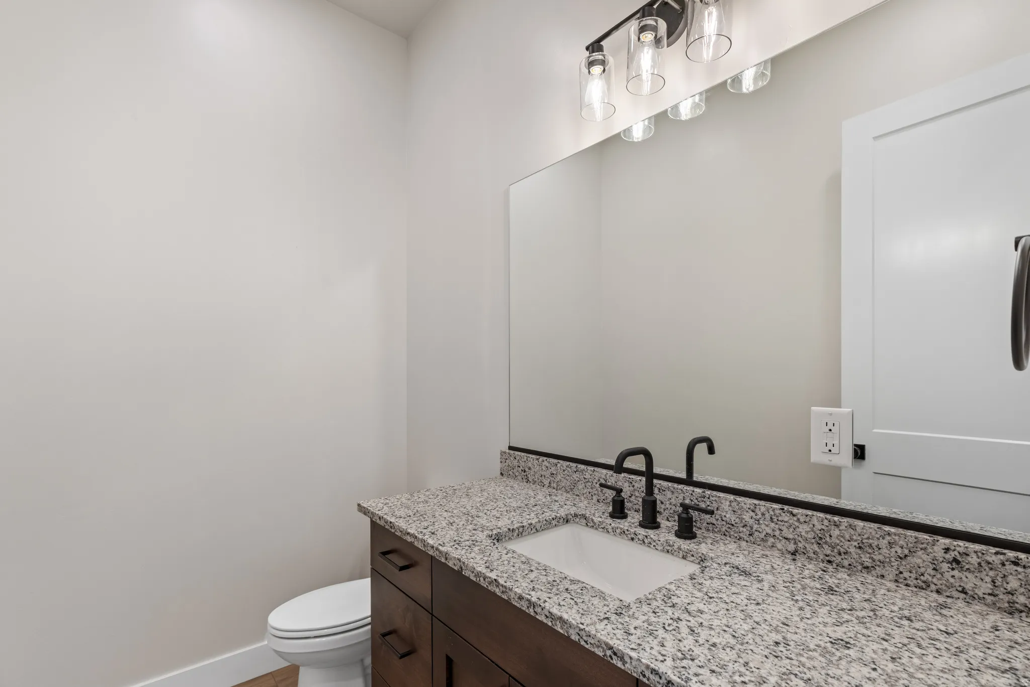 Granite countertop, undermount sink, dark wood-finish vanity, matte black fixtures, and a four-light vanity fixture