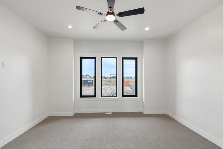 Recessed lighting, ceiling fan, white walls, gray carpet flooring, three black-framed windows