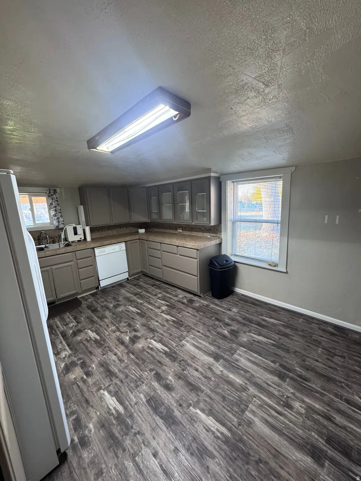 Kitchen with gray cabinetry, white appliances, healthy amount of natural light, dark wood-style flooring, and a textured ceiling