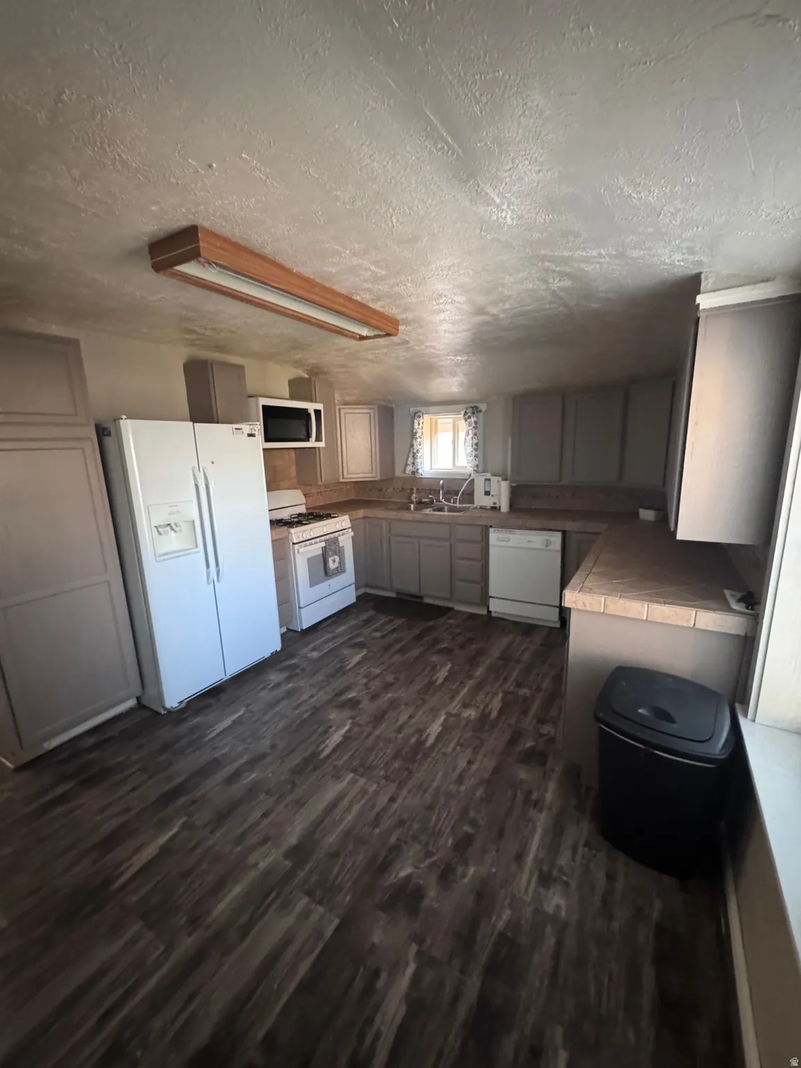 Kitchen featuring white appliances, tile countertops, dark wood-type flooring, a textured ceiling, and gray cabinetry