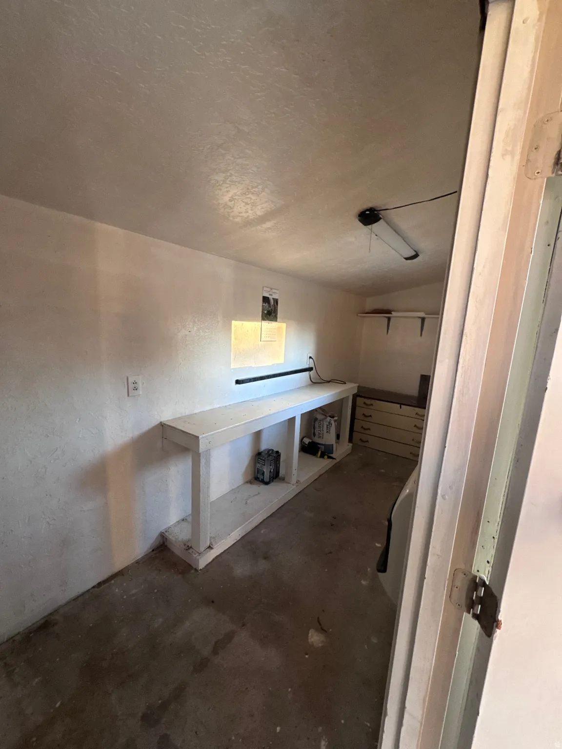 Bathroom with unfinished concrete floors, a textured wall, and a textured ceiling