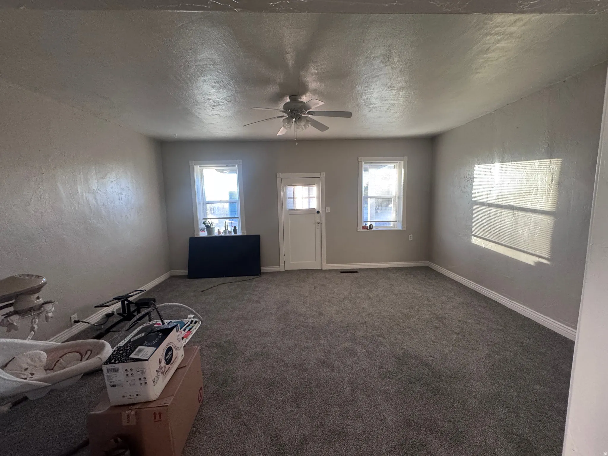 Unfurnished living room featuring a textured wall, carpet flooring, a textured ceiling, a ceiling fan, and plenty of natural light