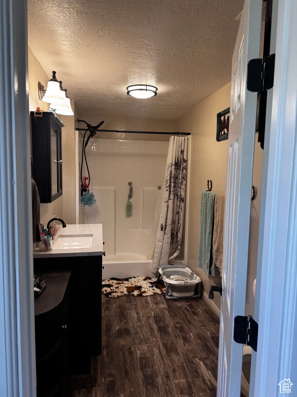 Full bathroom featuring vanity, shower / bathtub combination with curtain, wood finished floors, and a textured ceiling