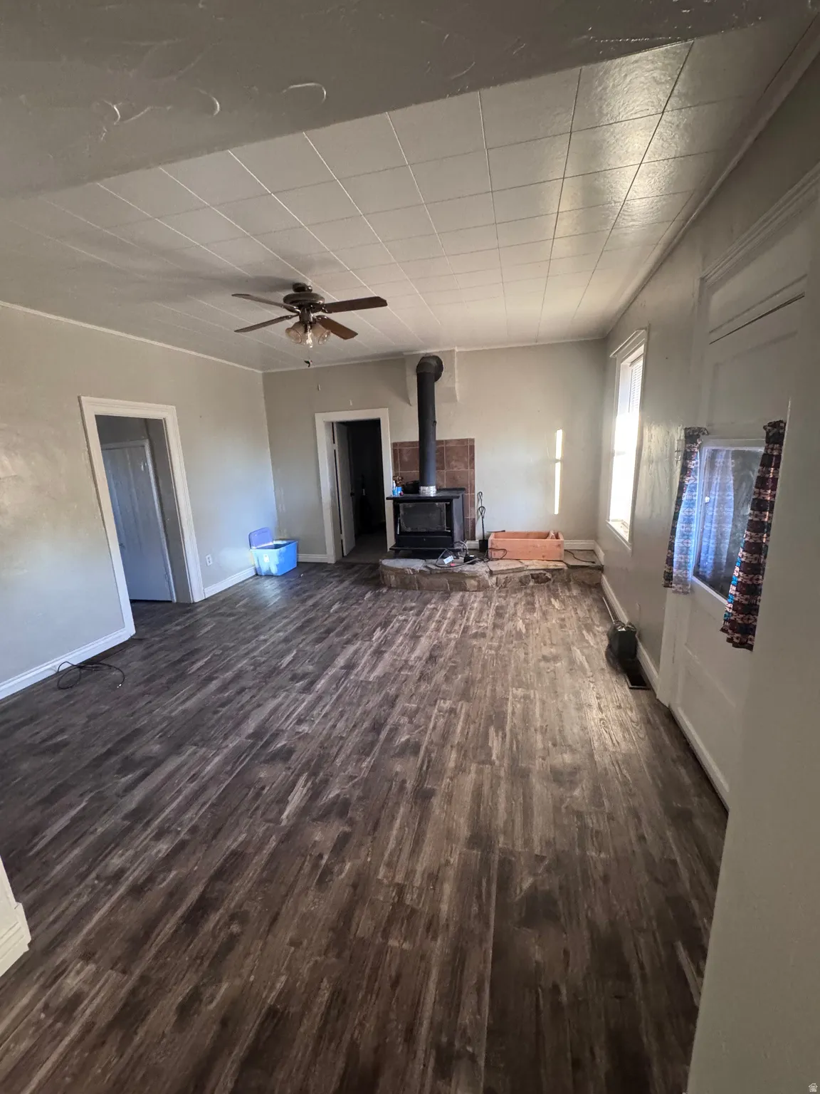 Unfurnished living room featuring ceiling fan, a wood stove, and dark wood-type flooring