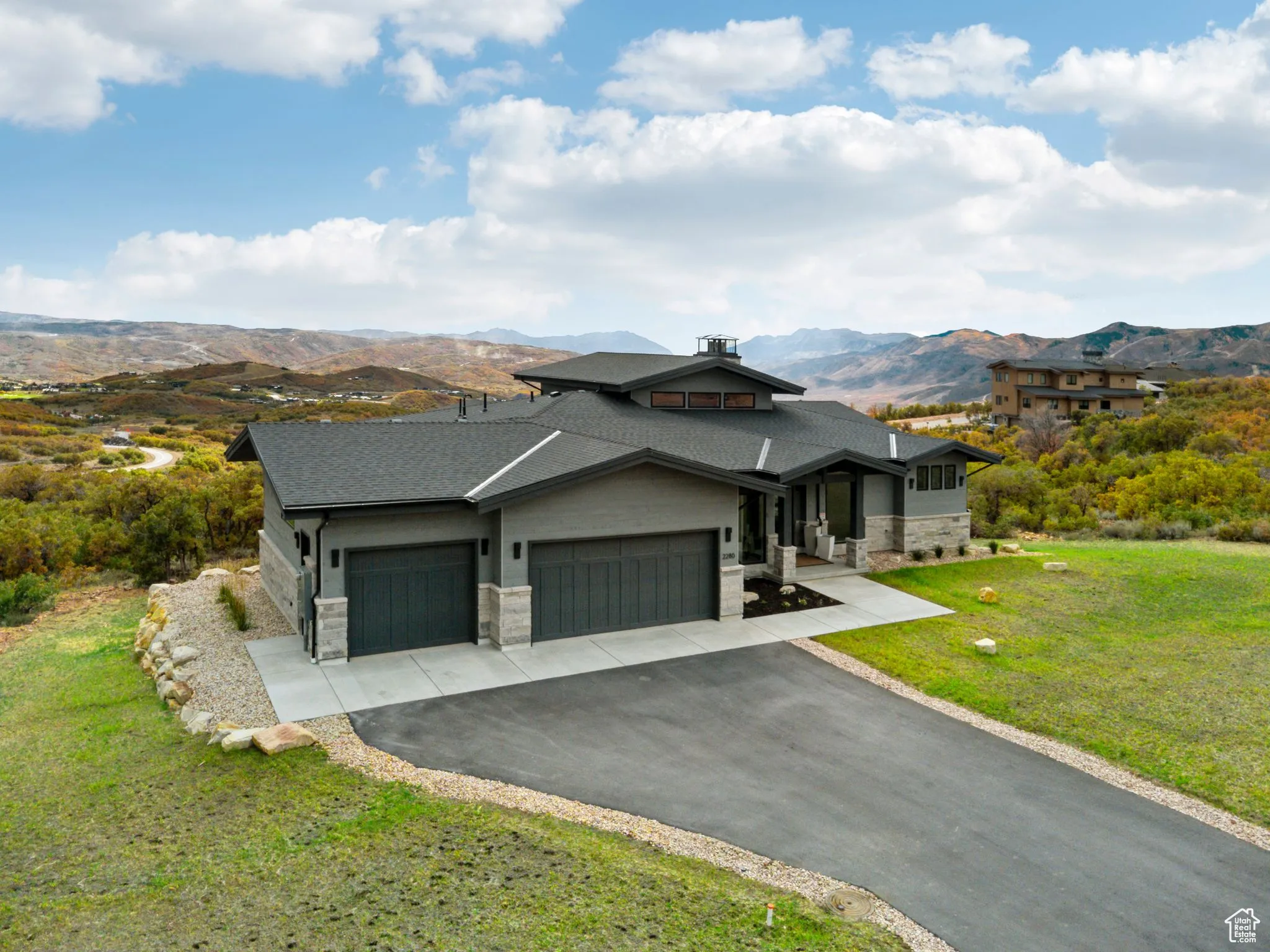 View of front of property with a front lawn, stone siding, an attached garage, and asphalt driveway