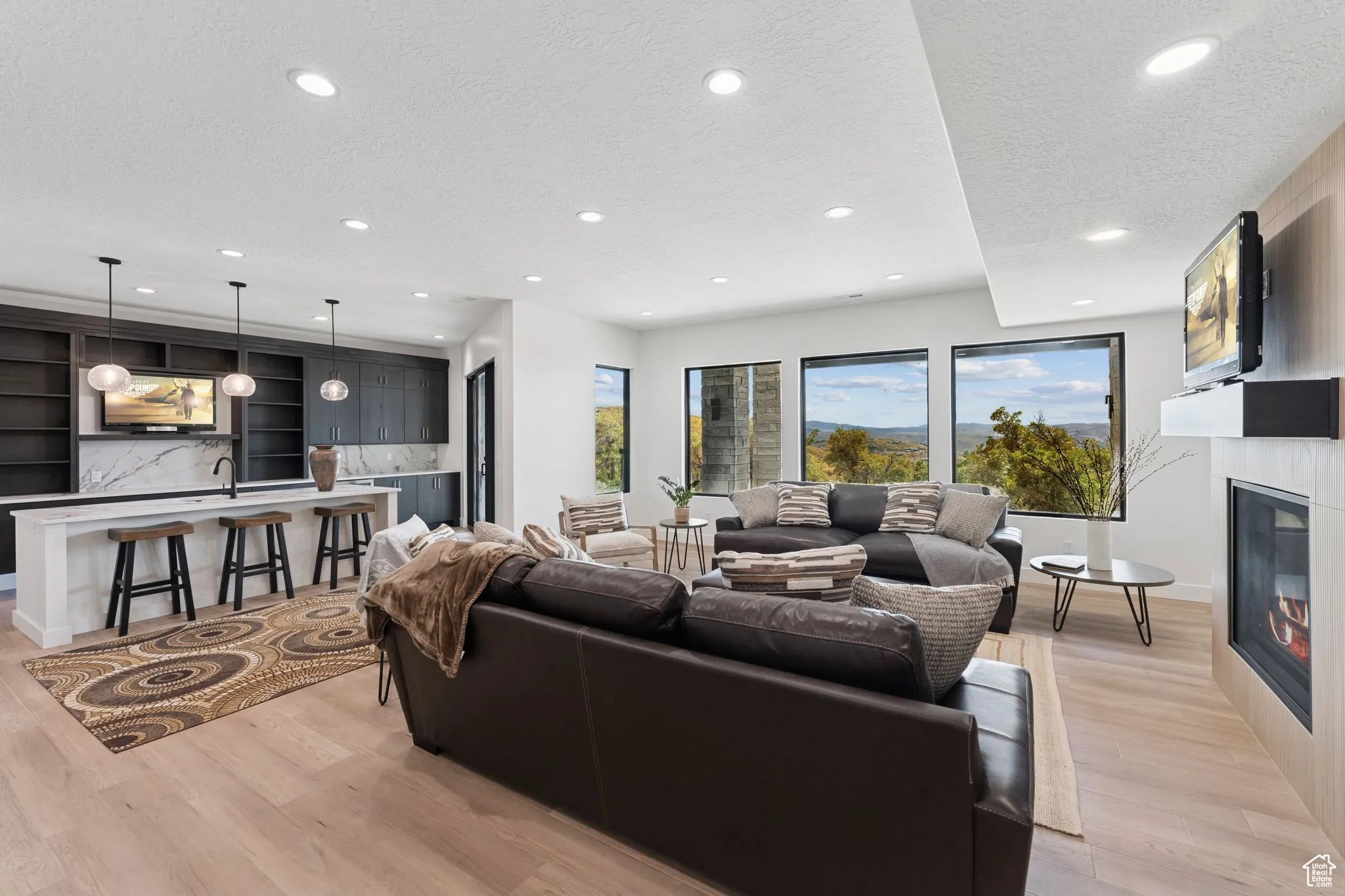 Living area featuring a textured ceiling, a glass covered fireplace, light wood-style flooring, and recessed lighting