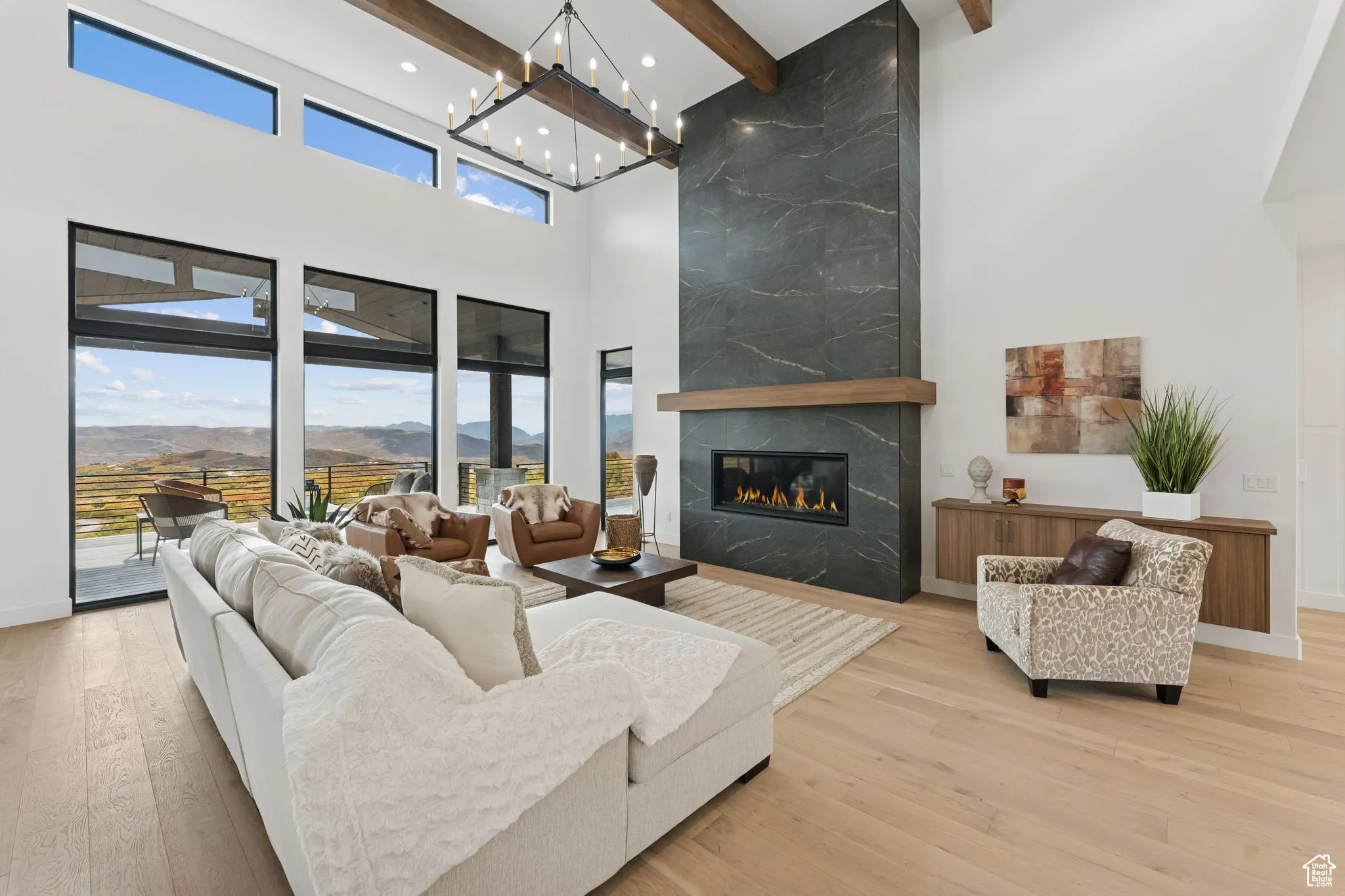 Living room featuring beam ceiling, a premium fireplace, light wood-type flooring, a high ceiling, and a mountain view