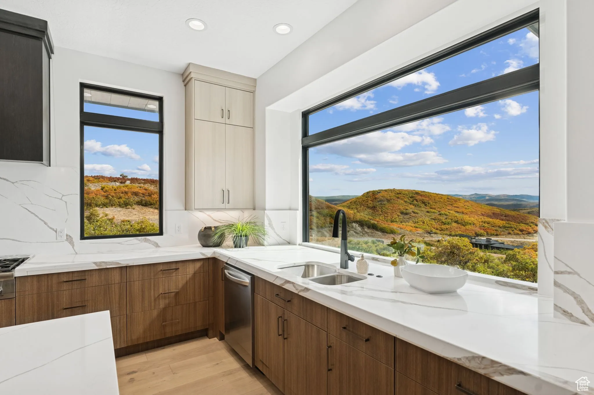 Kitchen featuring light stone counters, light wood finished floors, healthy amount of natural light, brown cabinetry, and recessed lighting