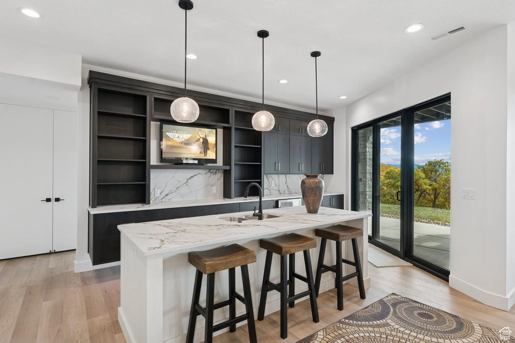 Kitchen with a breakfast bar, light stone counters, dark cabinets, decorative light fixtures, and recessed lighting