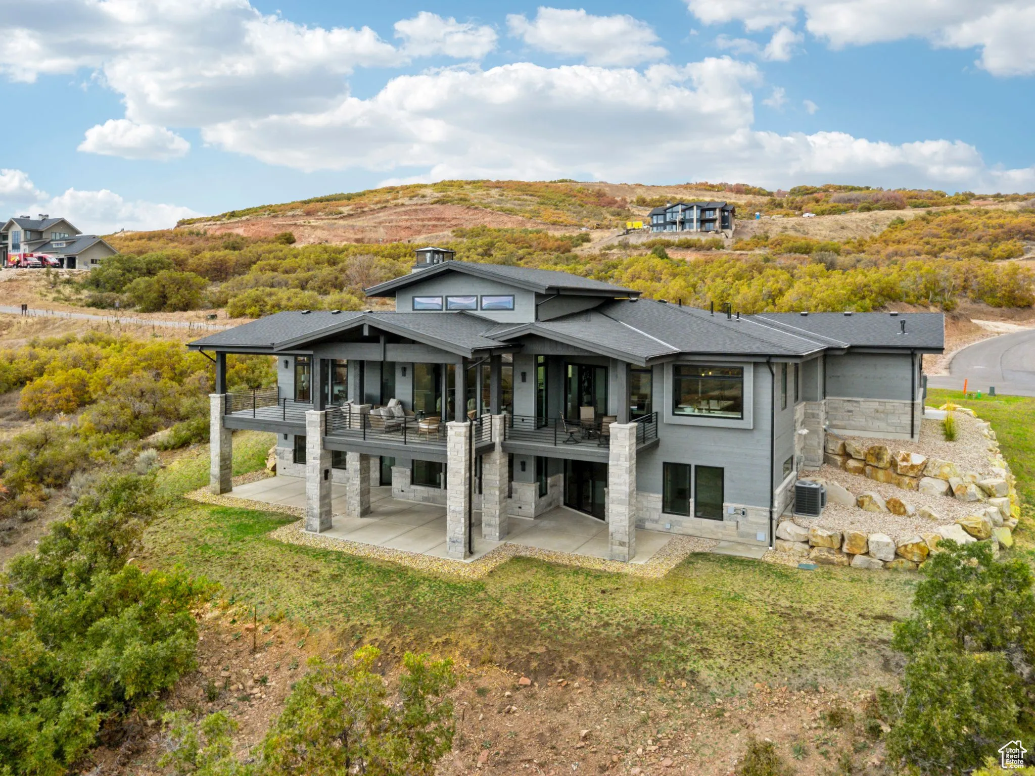 Back of house with a patio, stone siding, a shingled roof, and a lawn