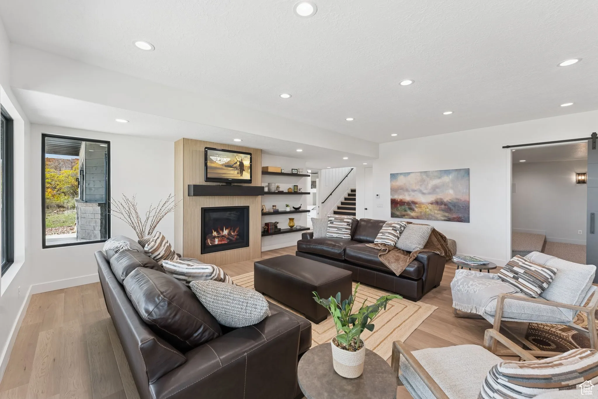 Living area with a barn door, recessed lighting, a large fireplace, light wood-style flooring, and stairway
