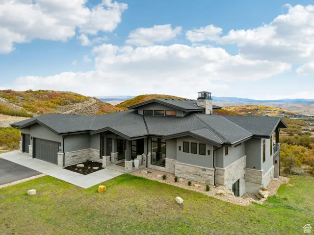 View of front of house with stone siding, a chimney, driveway, and a garage