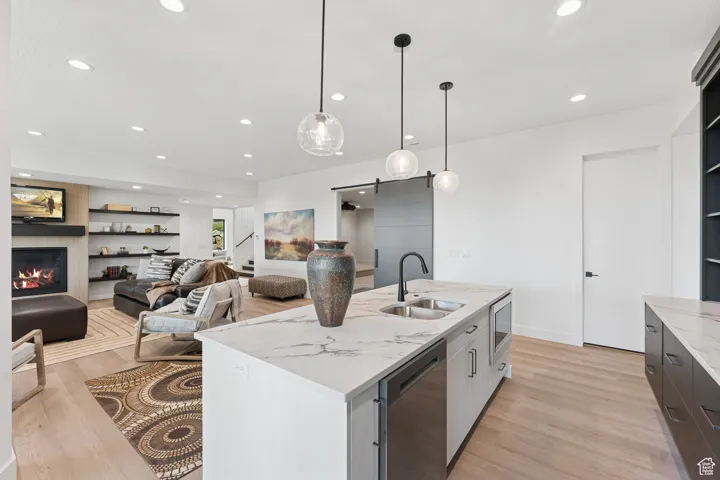 Kitchen with a barn door, decorative light fixtures, light stone countertops, light wood-style flooring, and recessed lighting