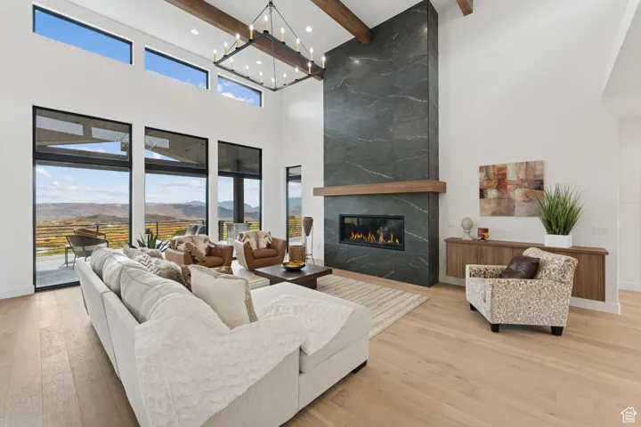Living room featuring beam ceiling, a premium fireplace, light wood-type flooring, a high ceiling, and a mountain view
