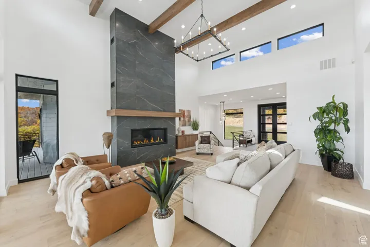 Living area featuring light wood finished floors, a fireplace, beamed ceiling, a towering ceiling, and recessed lighting