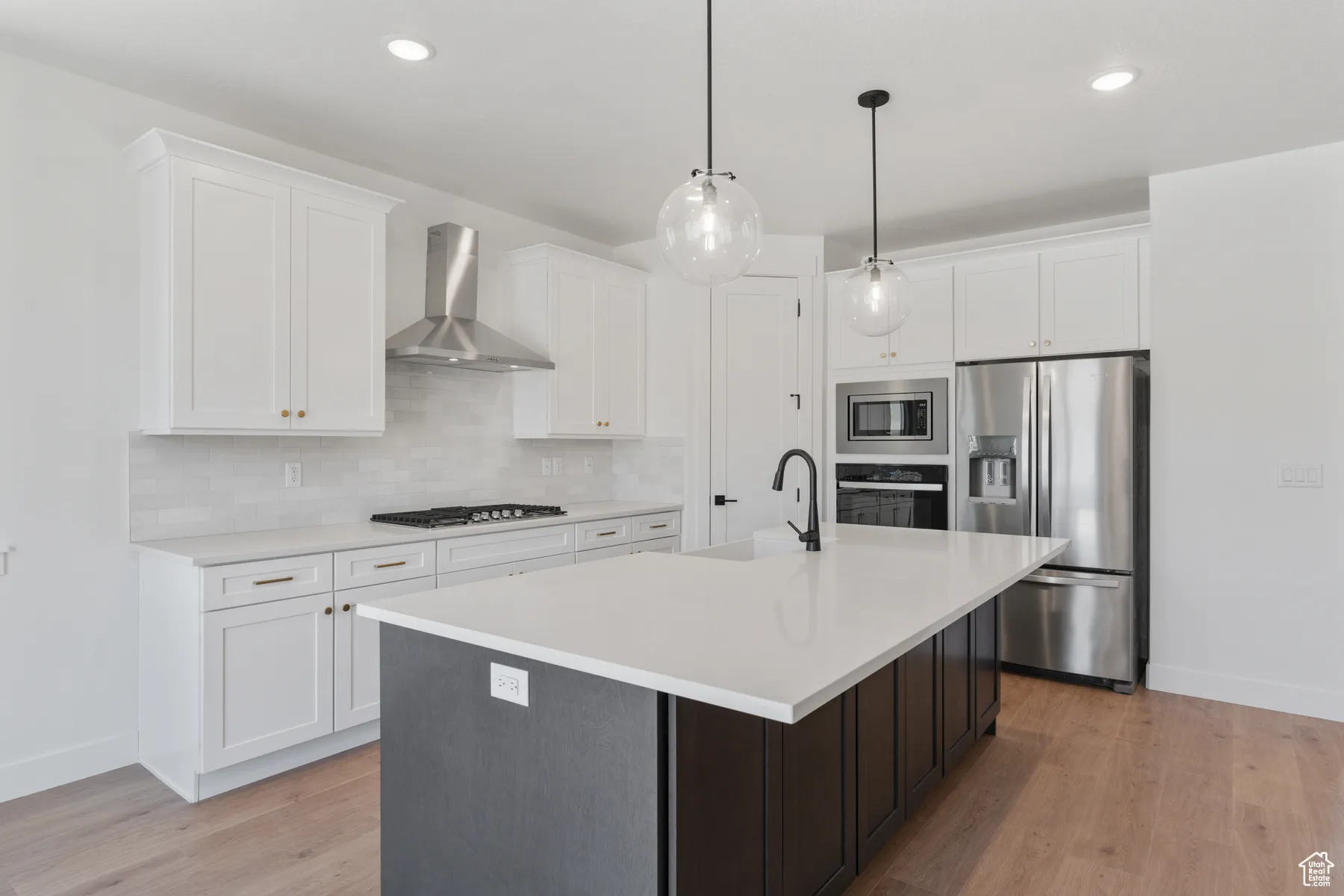 Kitchen featuring wall chimney range hood, appliances with stainless steel finishes, decorative backsplash, light countertops, and a center island with sink