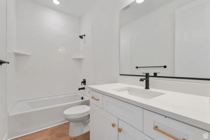 Bathroom with wood finished floors, vanity, shower / bath combination, and recessed lighting