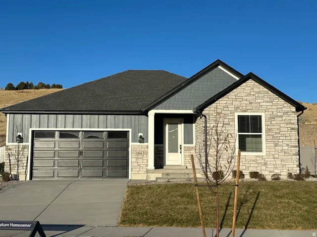View of front of house featuring stone siding, a front lawn, an attached garage, driveway, and board and batten siding
