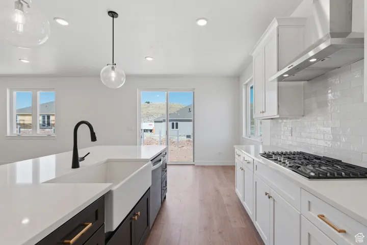 Kitchen with wall chimney range hood, stainless steel appliances, light countertops, backsplash, and recessed lighting