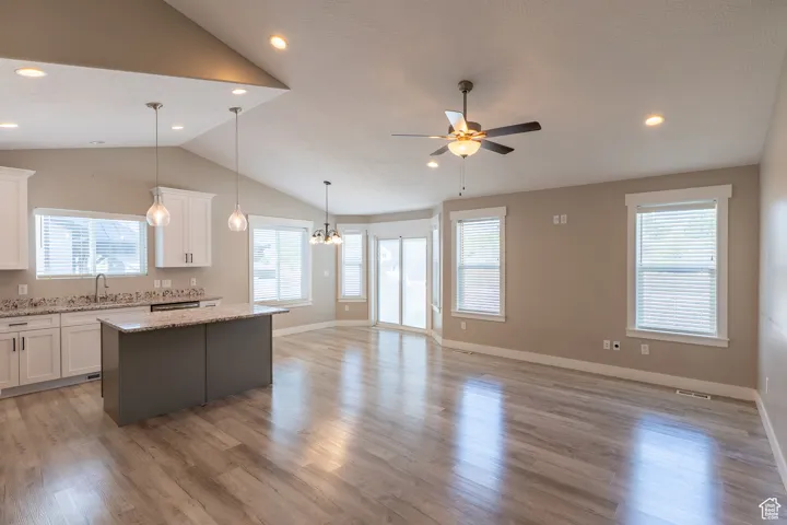 Kitchen featuring lofted ceiling, a kitchen island, a ceiling fan, open floor plan, and healthy amount of natural light