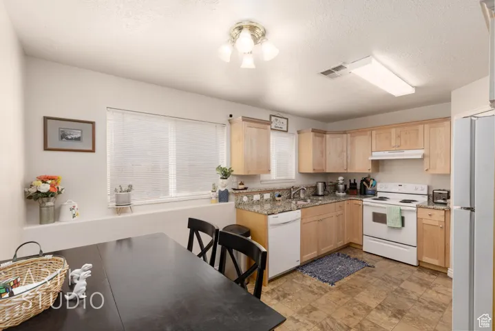 Kitchen featuring white appliances, light brown cabinets, under cabinet range hood, stone finish floors, and a textured ceiling