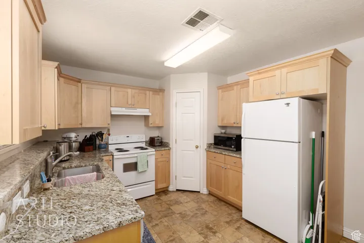Kitchen featuring white appliances, light brown cabinetry, under cabinet range hood, and light stone counters