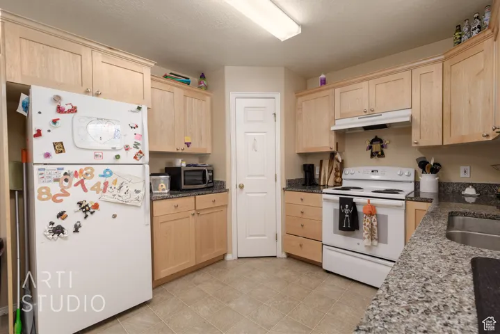 Kitchen with white appliances, light brown cabinetry, and under cabinet range hood