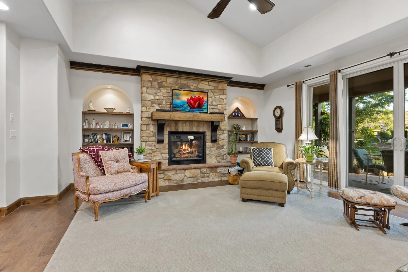 Living room featuring a stone-clad fireplace with wood mantel, vaulted ceiling, built-in arched shelving, and sliding glass doors to outdoor patio