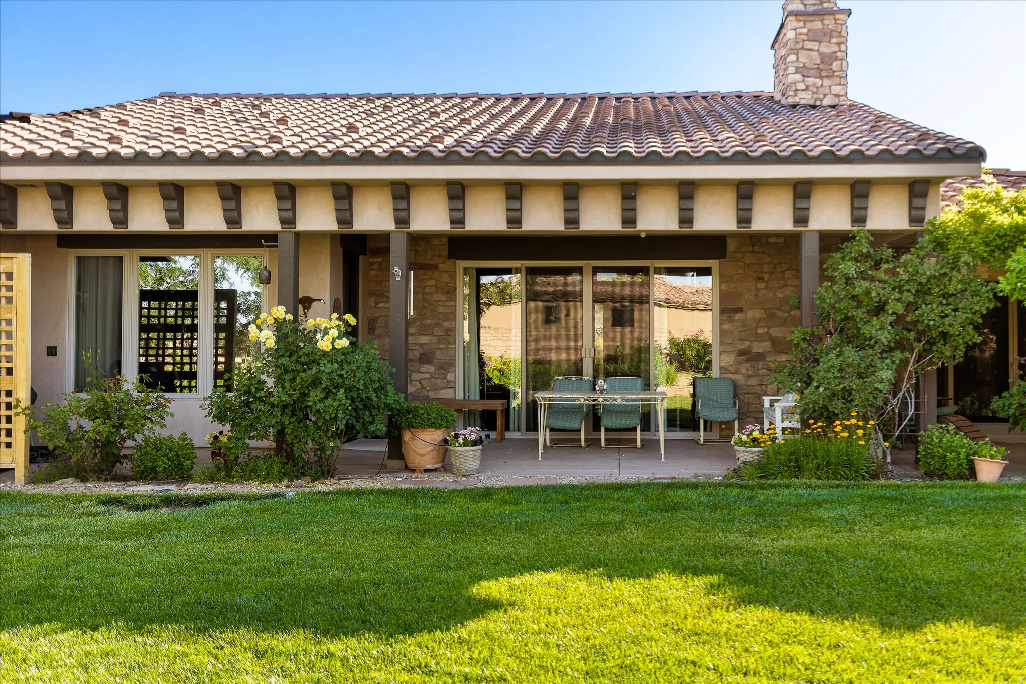 Expansive green lawn bordering a stone-clad exterior with a covered patio featuring sliding glass doors and a tile roof