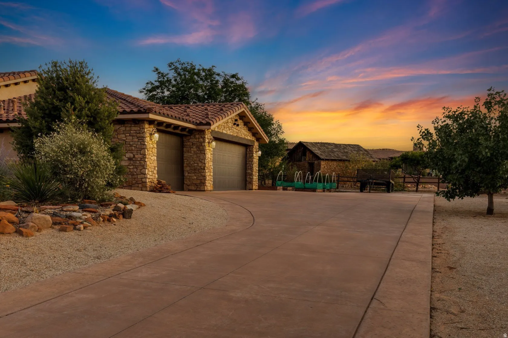 Stucco and stone facade home featuring a tile roof, two garage bays with dark doors, and exterior lighting fixtures