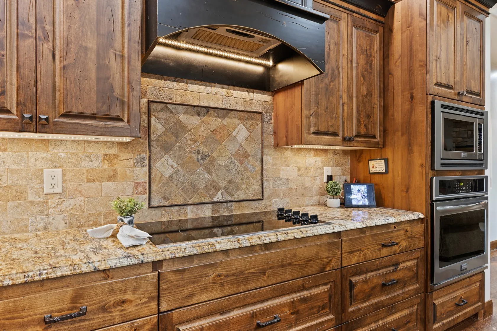 Kitchen featuring wood cabinetry, granite countertops, stone tile backsplash, and stainless steel built-in appliances
