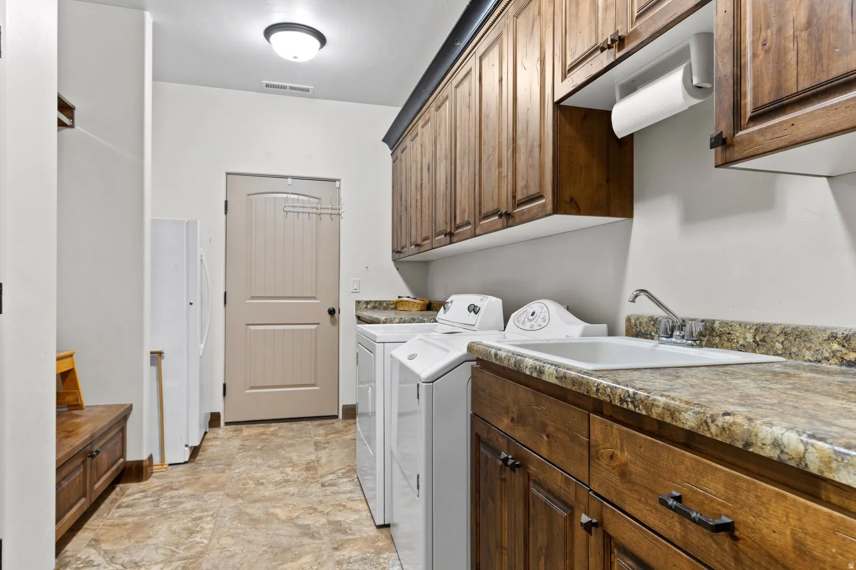 Laundry room featuring wood cabinetry, a utility sink, and stone-finish countertops