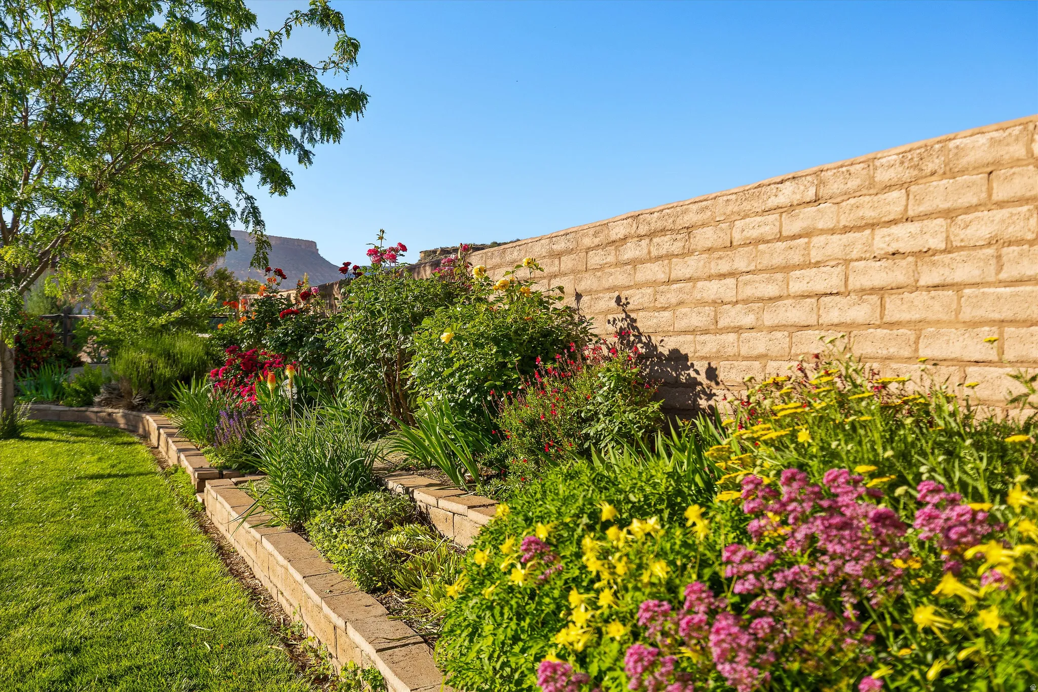 Manicured lawn with a tiered garden bed featuring various flowering plants and shrubbery