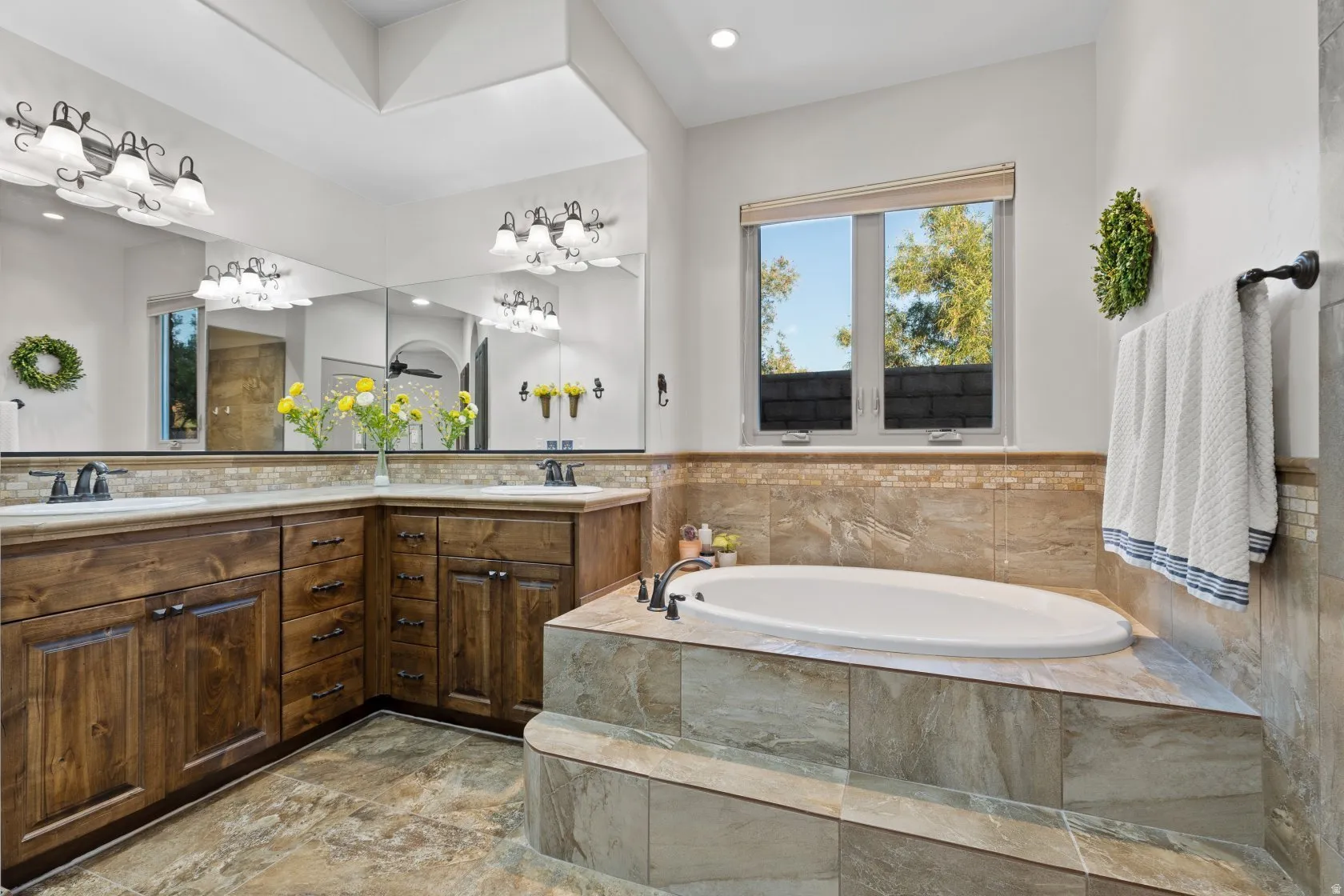 Expansive bathroom featuring a built-in soaking tub with stone surround, a dual vanity with wood cabinetry and undermount sinks, and a large wall-mounted mirror