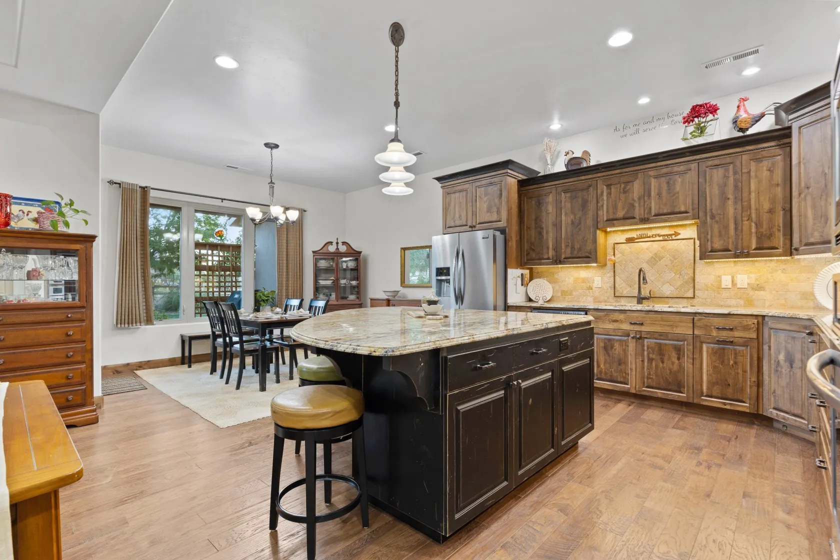 Open-concept kitchen and dining area featuring wood-finish flooring, a kitchen island with stone countertop, dark wood cabinetry, stainless steel appliances, and recessed lighting
