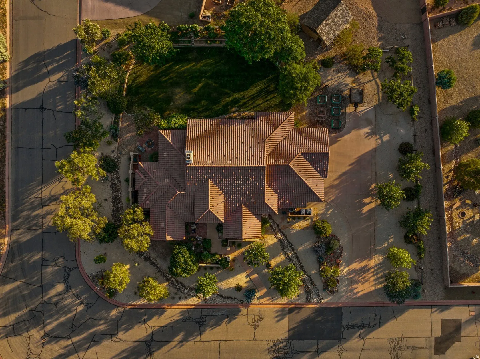 Expansive property featuring a multi-gabled tile roof, a large unpaved parking area, extensive desert landscaping, and a fenced grass lawn