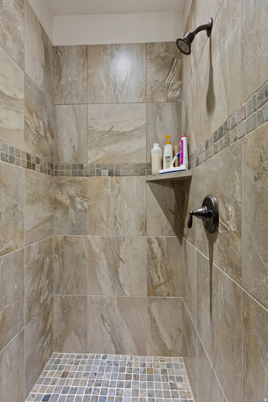 Tile shower enclosure featuring a multi-tone mosaic accent band