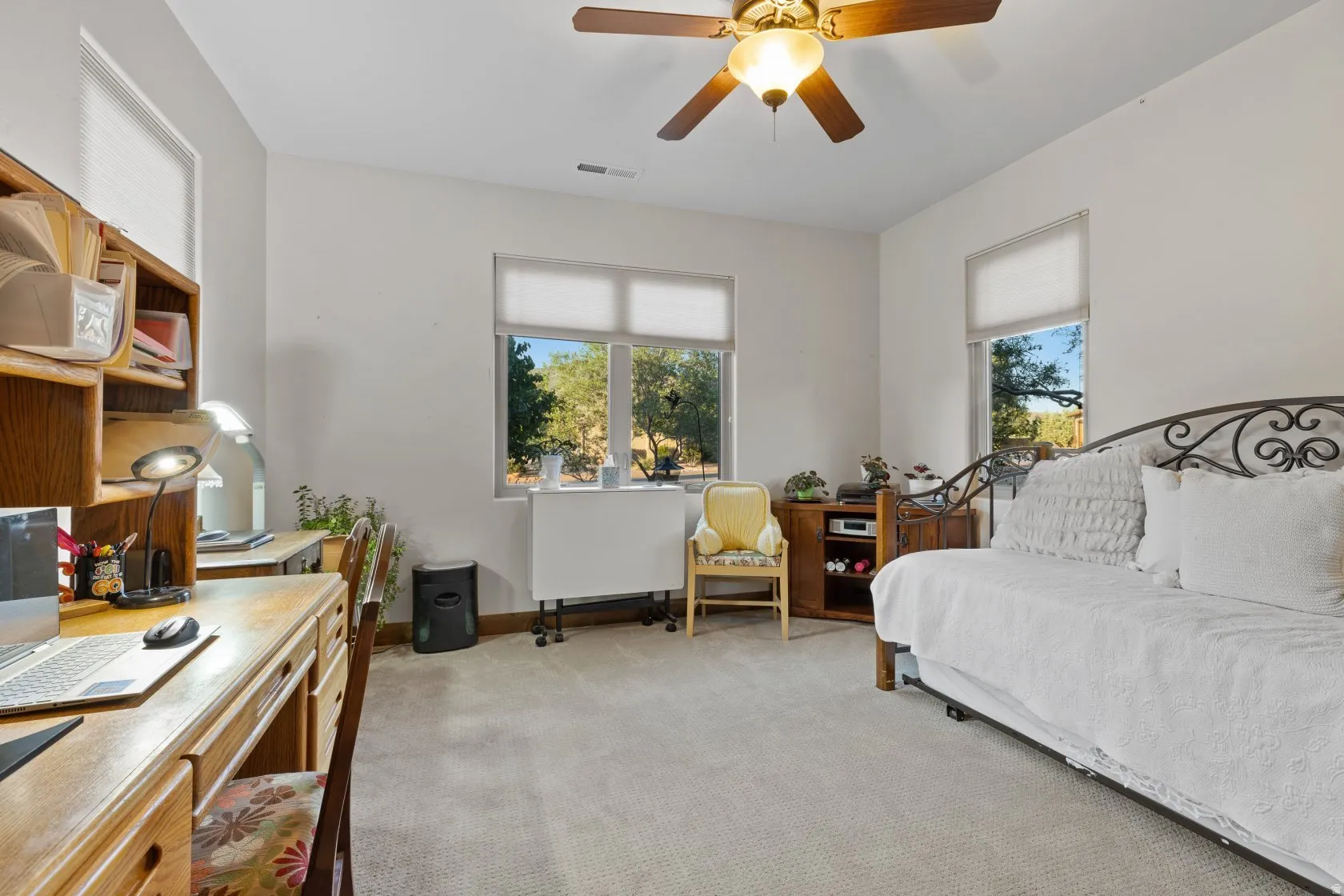 Bright interior room featuring a ceiling fan with integrated lighting, multiple windows with roller shades, and light-toned carpet flooring