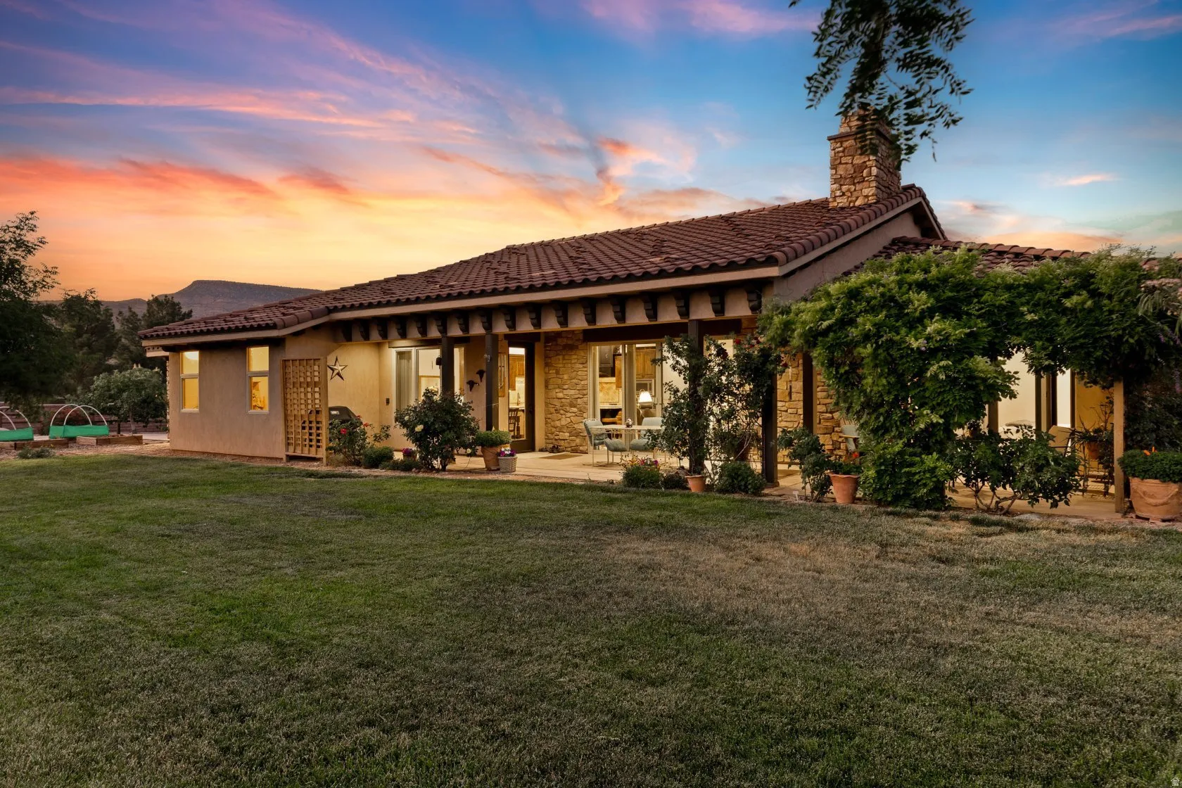 Spanish Colonial-style residence featuring a red tile roof, stucco exterior, stone accent walls, a covered patio with columns, and a stone chimney