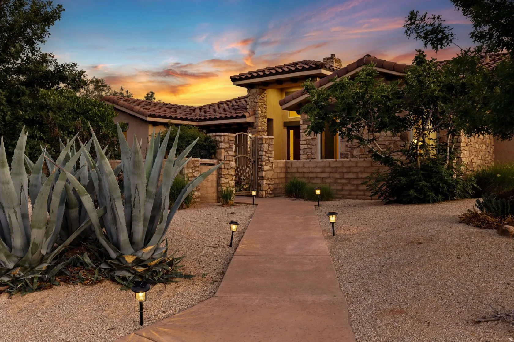 Stucco and stone exterior featuring a concrete pathway, landscape lighting, and mature plantings