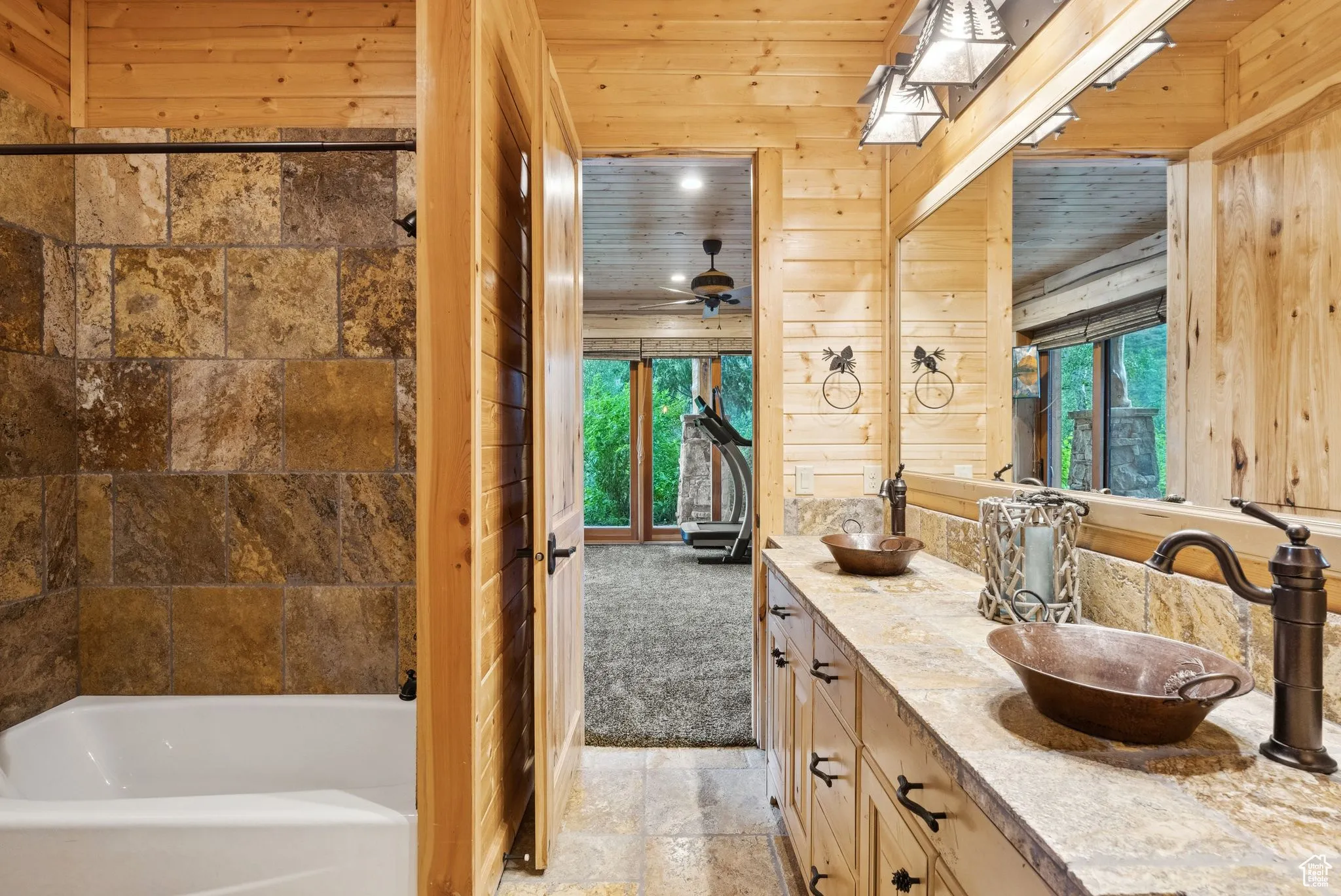 Bathroom featuring wood walls, stone tile flooring, plenty of natural light, and double vanity