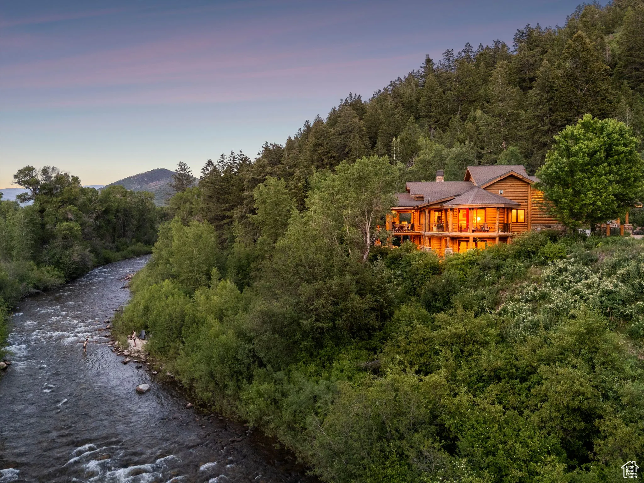 Back of property at dusk featuring a chimney, a view of trees, and a wooden deck