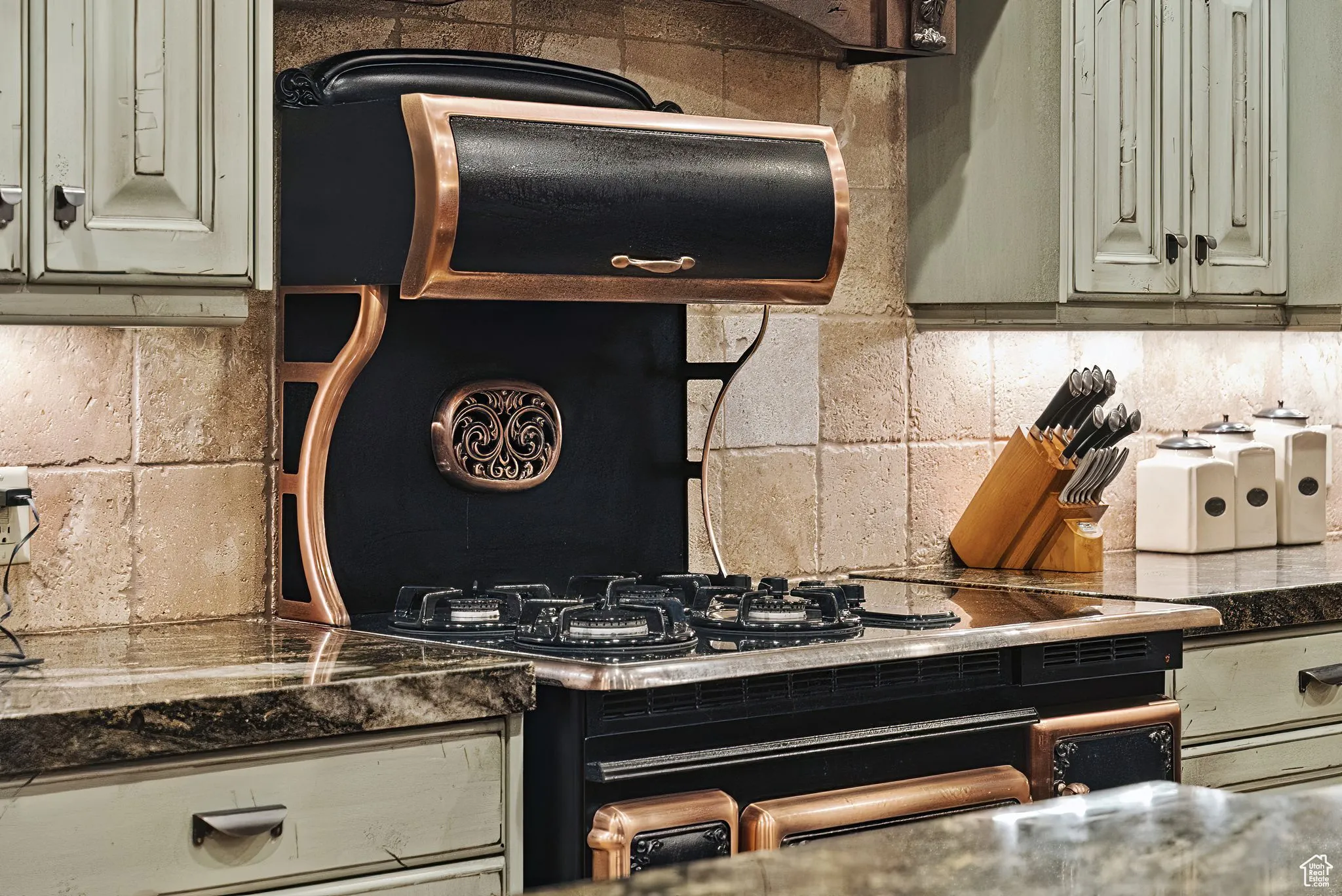 Kitchen with sage cabinets, tasteful backsplash, and dark countertops