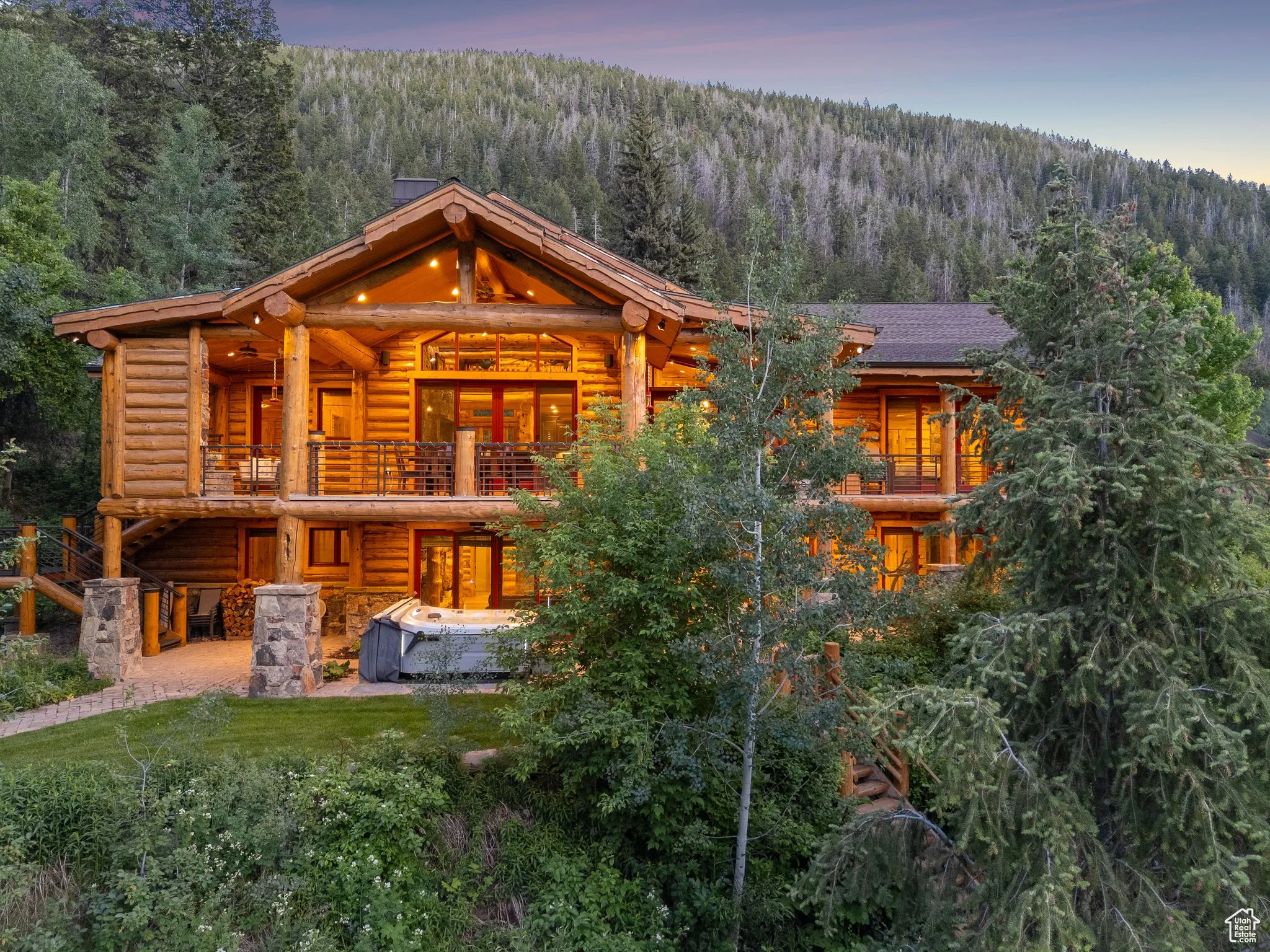 Back of property featuring a forest view, split-log veneer framed home, a balcony, and a patio