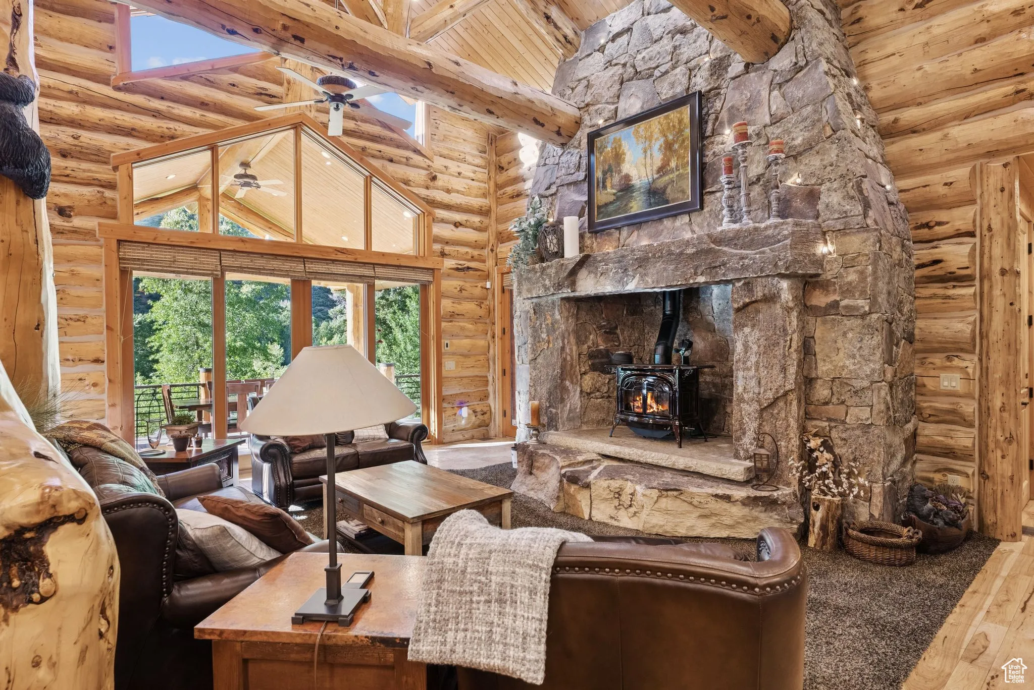 Living area with rustic walls, a remote operated propane stove, wood flooring, high vaulted ceiling, and ceiling fan