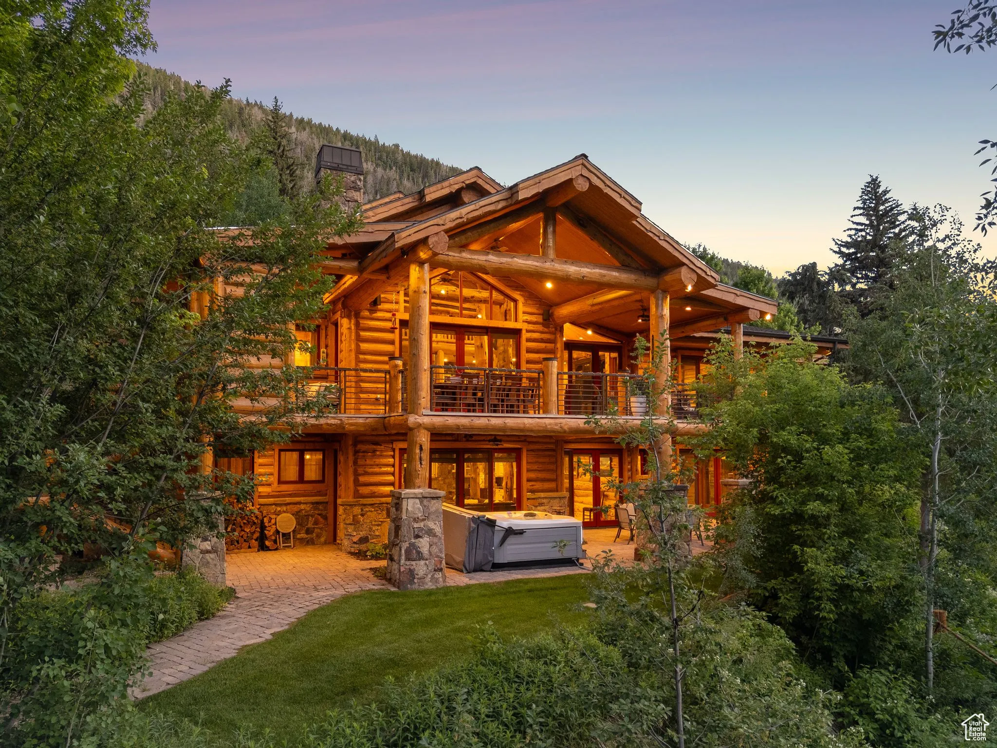 Back of split-log veneer, framed home featuring a hot tub, a balcony,  a patio area, and a chimney